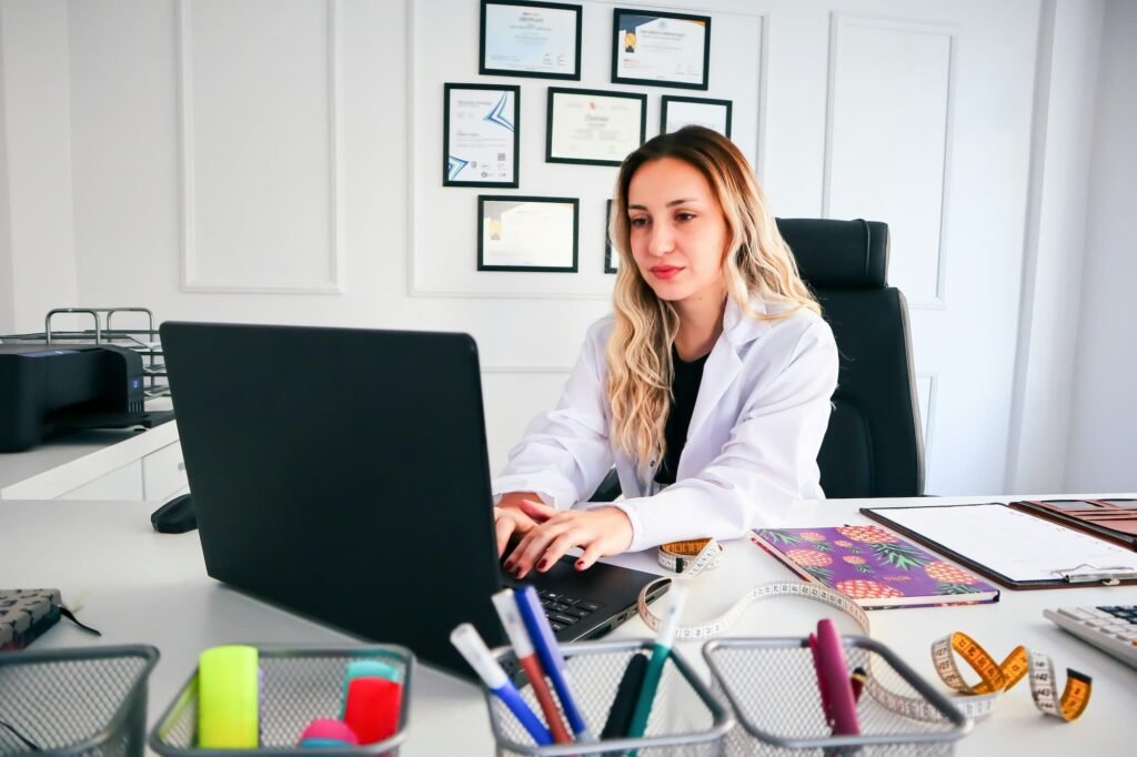 Med spa clinic owner in white coat working on an AI-ready service page with credentials on the wall behind her