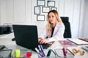 Med spa clinic owner in white coat working on an AI-ready service page with credentials on the wall behind her